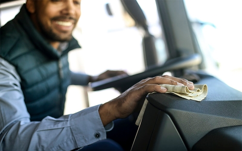 A truck driver wiping down their dashboard with a beige rag. 