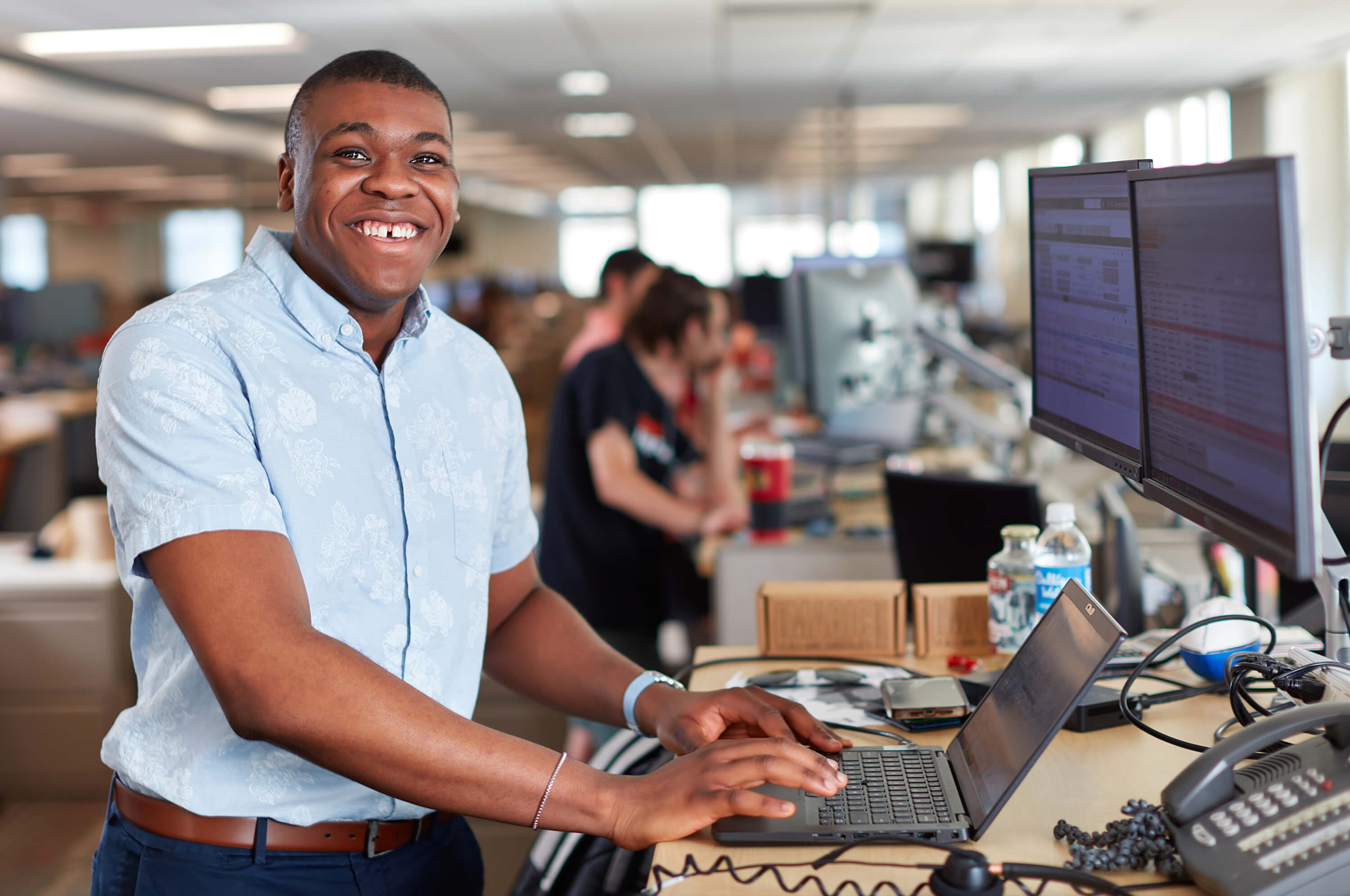 A Schneider office associate standing at his desk with several associates in the background working