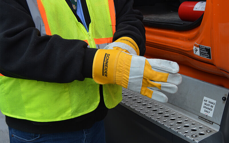A Schneider truck driver slips on a pair of canvas work gloves with the company logo.
