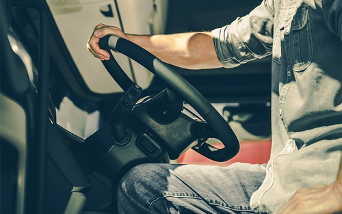 A truck driver with their hand on the steering wheel.