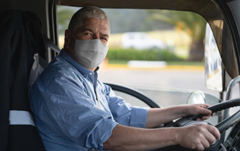A truck driver wears a cloth face mask while behind the wheel.
