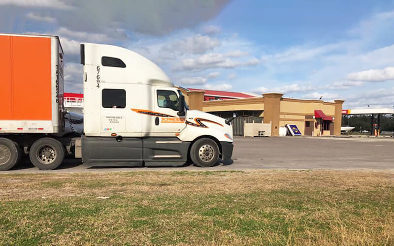 A Schneider semi-truck is parked outside of a truck stop.