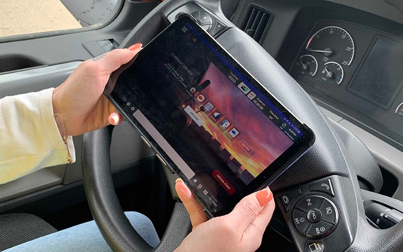 A female driver holds a Schneider tablet in her hands while sitting in the driver's seat of a semi-truck.