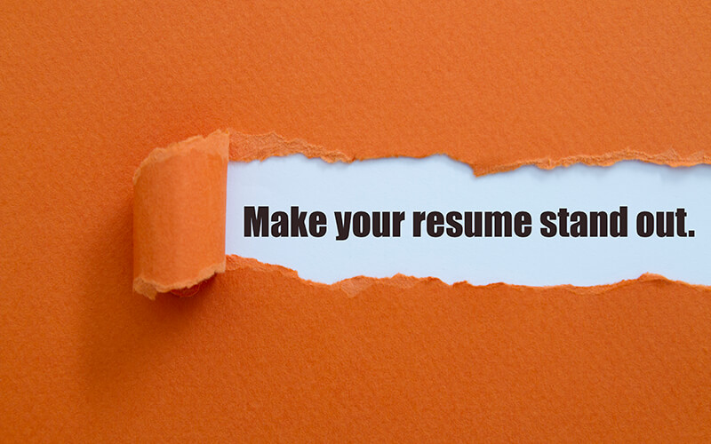 A piece of orange paper is ripped out of a larger piece of orange paper and within the ripped part are the words, "Make your resume stand out."