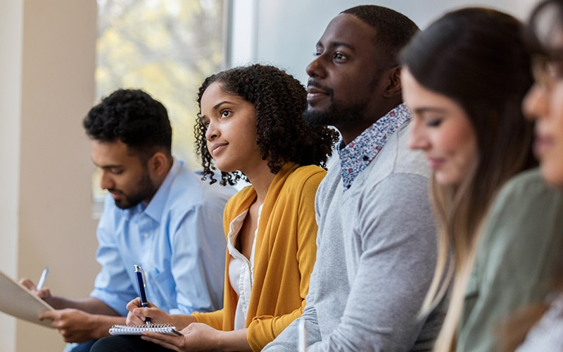 A group of people sitting in chairs and taking notes.