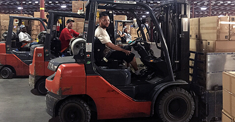 Three Schneider associates line their forklifts up to lift pallets of cargo in a company warehouse