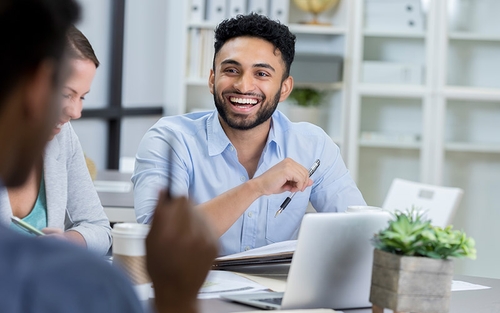 A man sitting at a table holding a pen and smiling at someone across from him.