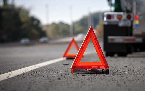 Two orange and reflective emergency triangles sit behind  truck that has pulled over to the shoulder of a highway.