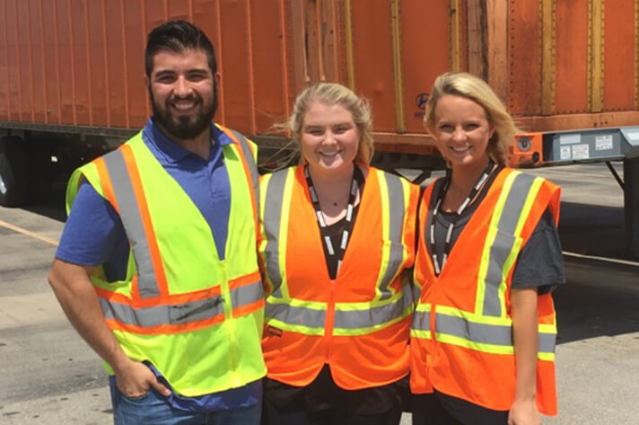 Three Schneider interns pose together while wearing safety vests in an intermodal yard