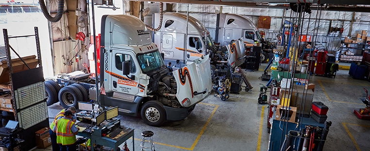 Two Schneider company trucks are positioned outside the doors of the service bays at a company diesel shop