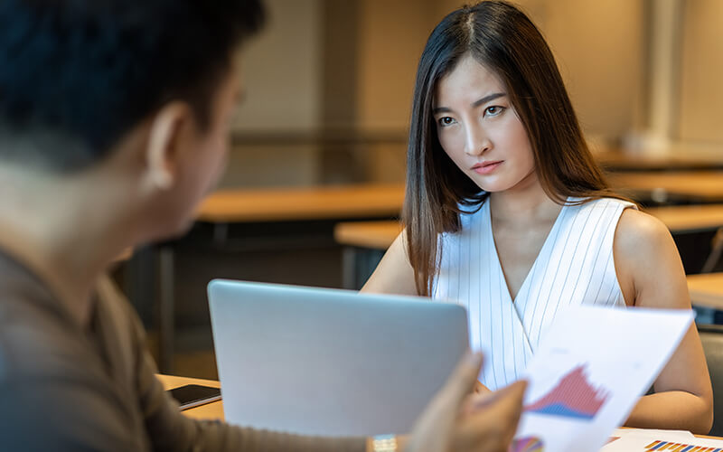 An associate appears upset while glancing up from her computer to look at colleagues across the table.