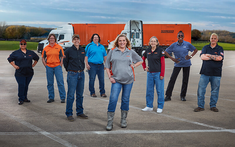 A group of Schneider female truck drivers pose in front of a company truck.