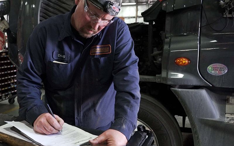 A Schneider diesel technician checks items off on a truck inspection checklist.