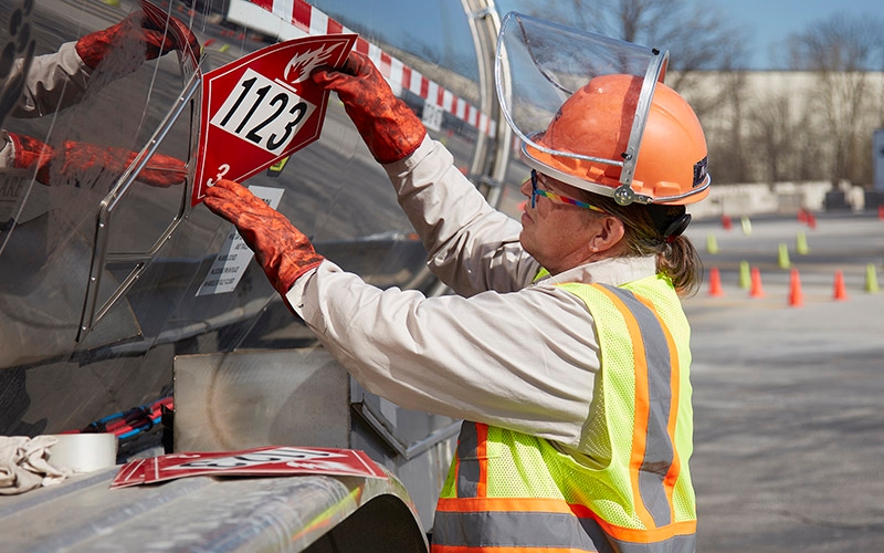 A Schneider truck driver placing a placard on their tanker trailer.