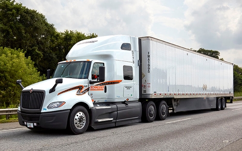 A Schneider semi-truck hauling a white Dedicated trailer under a cloudy sky.