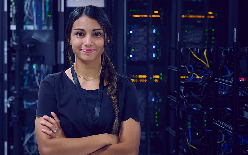A woman standing and smiling with her arms crossed in front of a server room.