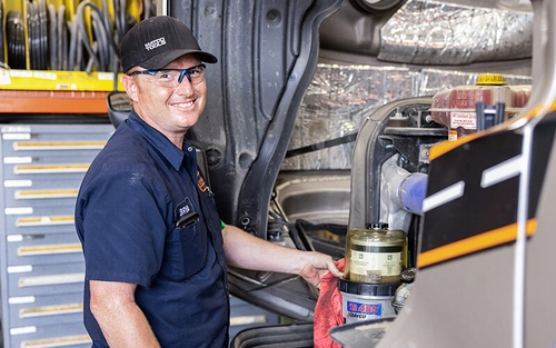 Schneider diesel technician wiping down a fuel filter with a rag while working under the hood of a semi-truck in the shop.
