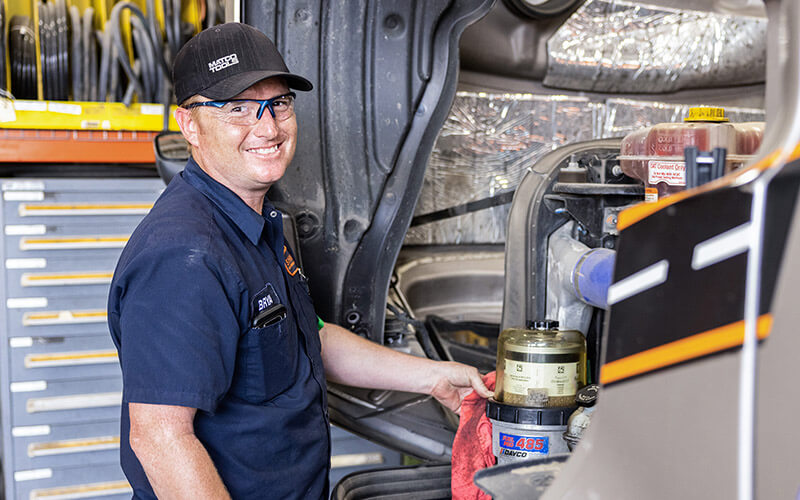 Schneider diesel technician wipes down a fuel filter with a rag while working under the hood of a semi-truck in the shop.