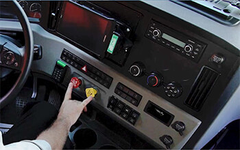Driving Instructor Brett shows where the brakes, which are a red and a yellow button, are on the dashboard of a semi-truck.
