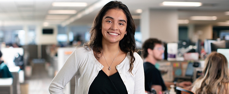 A Schneider office associate smiles with other associates working at their desks are blurred in the background behind her