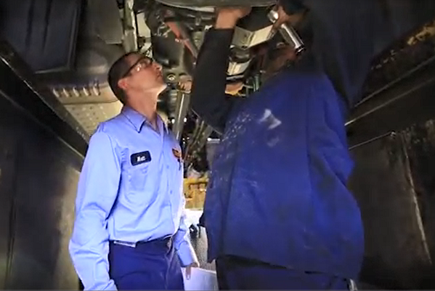 Schneider diesel technicians work on the underbody of a truck from inside a pit
