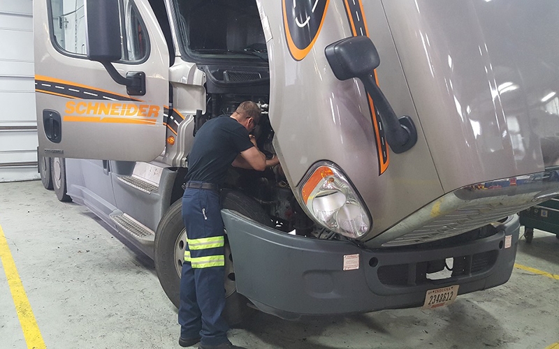 A Schneider lead technician works under the hood of a company truck.