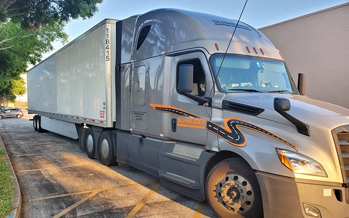A grey Schneider semi-truck hauling a white trailer is parked outside of a business.