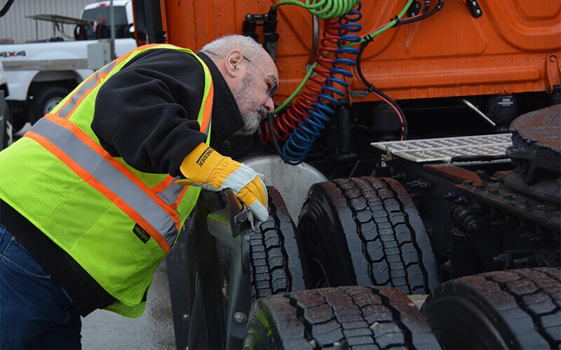 A driver grabs the side of his truck with gloved hands during a pre-trip inspection.
