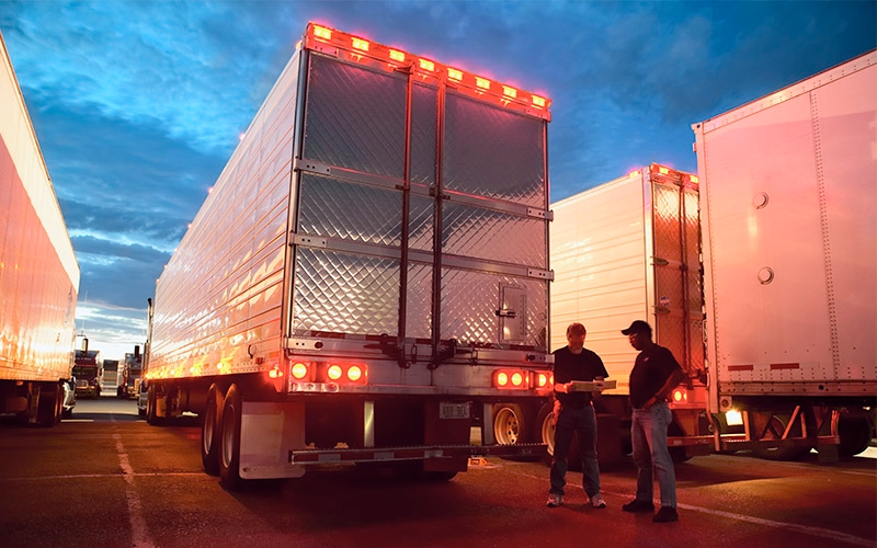 Two truck drivers talking outside of a semi-truck at night.