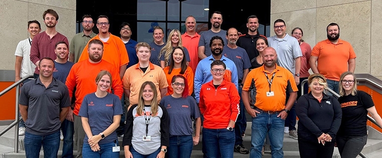 A diverse group of Schneider associates stand on the steps of Schneider's corporate office.