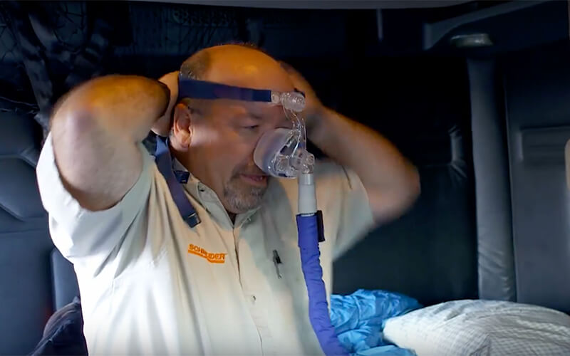 A truck driver puts on a CPAP machine by placing the mask over his nose and securing the straps behind his head.