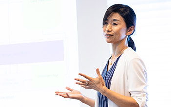 An associate gestures with palms up and hands open to emphasize her point while giving a business presentation.