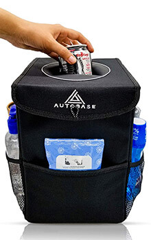 A hand places a can inside a travel garbage can. The garbage can has pockets on each side holding various toiletries.