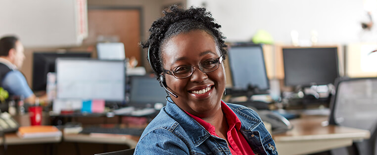 A Schneider customer service associate smiles while wearing a headset in her office area at a Schneider facility