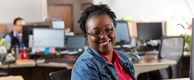 A Schneider customer service associate smiles while wearing a headset in her office area at a Schneider facility