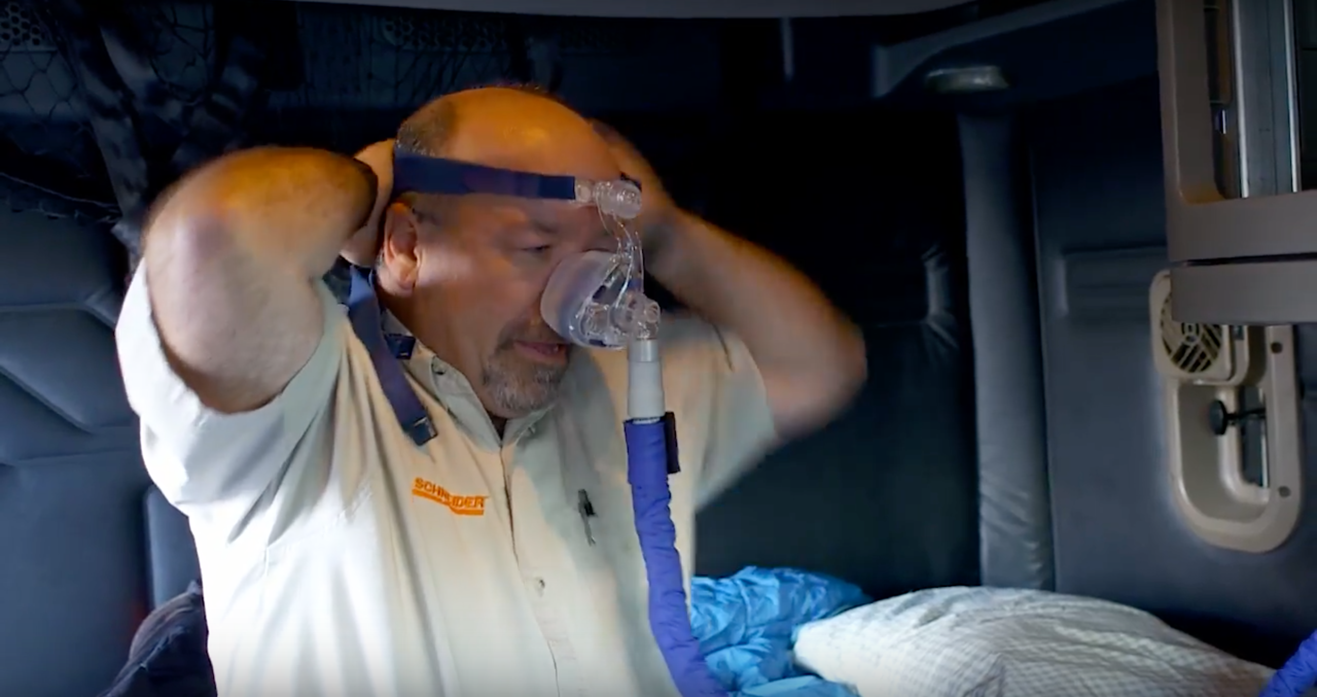 A Schneider driver shows how to put on a CPAP mask by putting the mask over his nose and securing the straps along the back of his head.