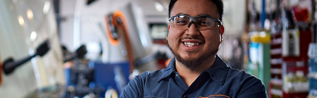 A Schneider diesel technician smiles brightly while wearing safety glasses on the shop floor