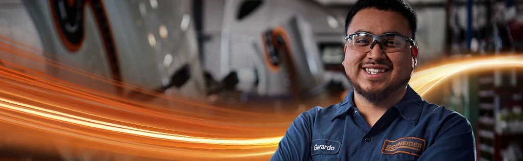 A Schneider diesel technician smiles brightly while wearing safety glasses on the shop floor