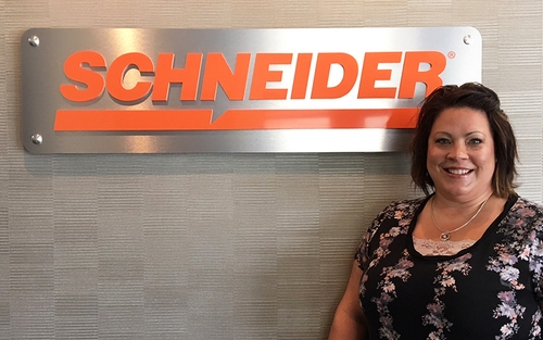 Jolene poses with the Schneider logo on the wall of a company facility.