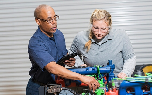 A man showing a woman various components on a diesel engine.