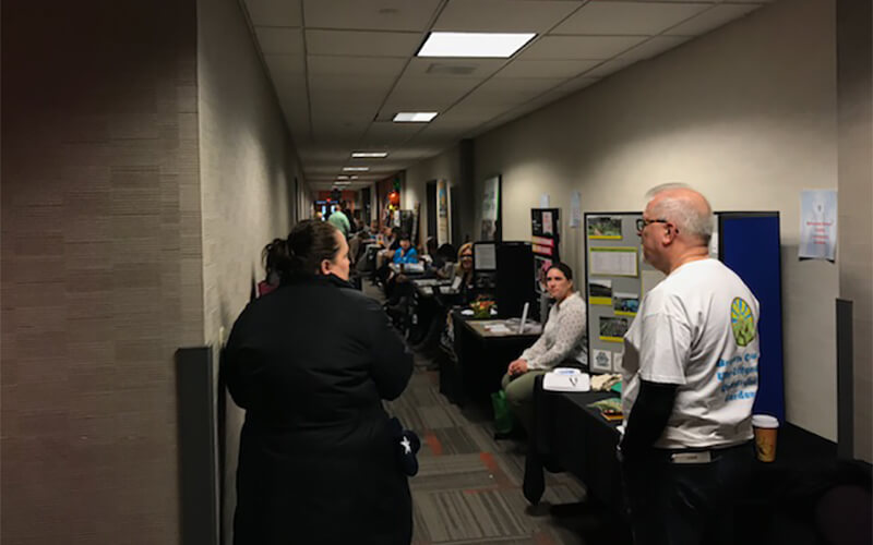 A busy hallway in a Schneider office is lined with Volunteer Fair booths and representatives from local non-profit organizations.