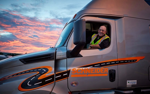 A Schneider driver leans out of a semi-truck window at sun rise.