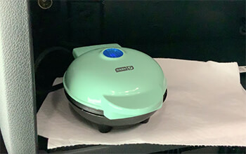 A mint green Dash Mini Waffle Maker sits on top of a paper towel on the counter inside a sleeper semi-truck.