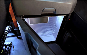 A grey mini-fridge is located behind the passenger seat on the inside of a semi-truck.