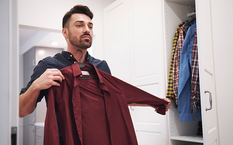 A man holding up a shirt while looking in the mirror.