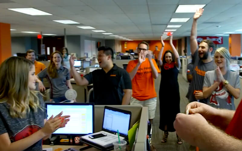 A team of Schneider office associates clap and cheer enthusiastically in a team meeting