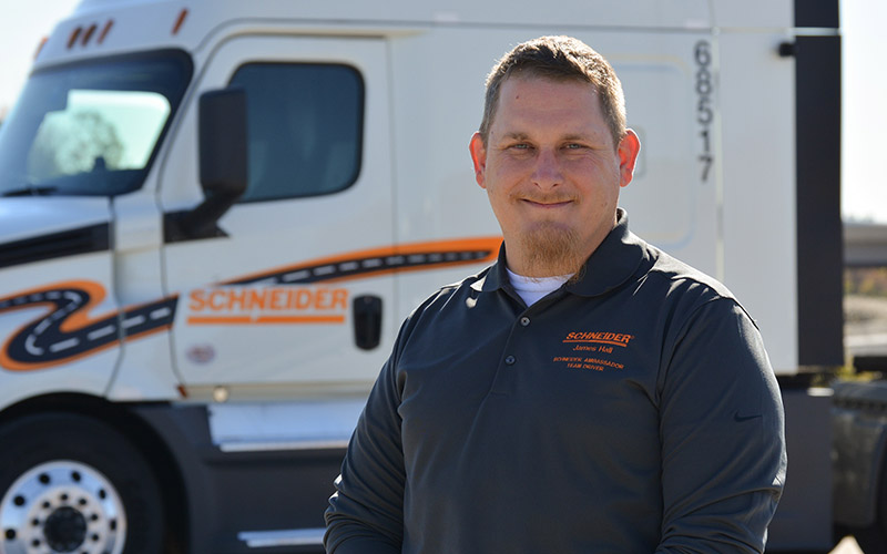 James Hall standing outside in front of a Schneider semi-truck, smiling forward.