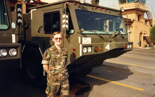 A young David Buck stands in front of a U.S. Air Force vehicle in uniform 