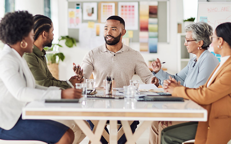 A group of five individuals sit at a table and have a discussion.