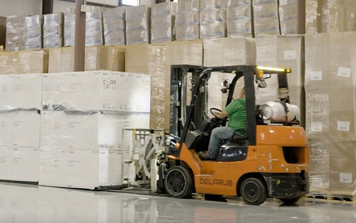 A warehouse associate operates a forklift to lift palettes. 